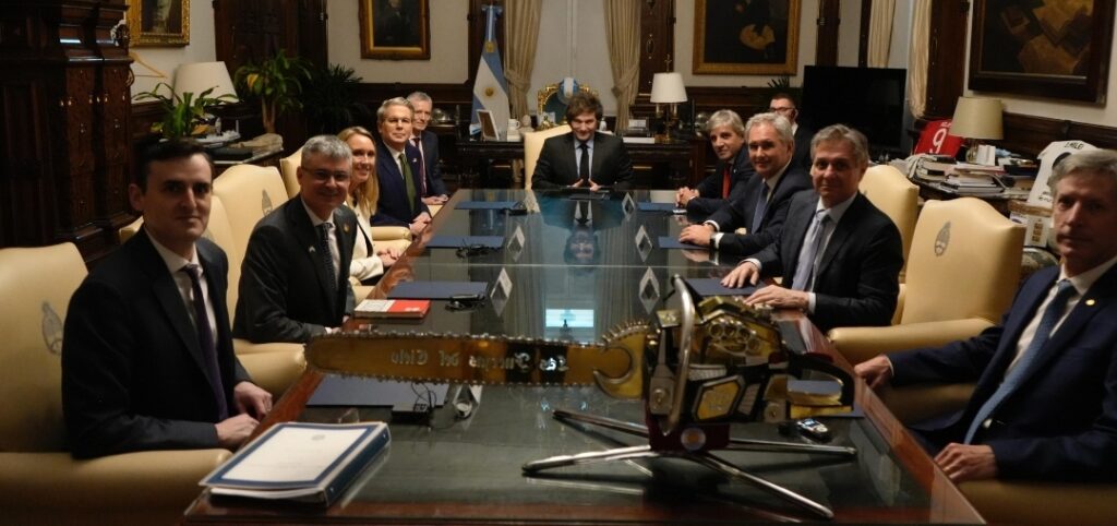 Scott Bessent en la Casa Rosada, sentado ante la mesa encabezada por Javier Milei, junto al equipo económico argentino y la motosierra en primer plano de la imagen.